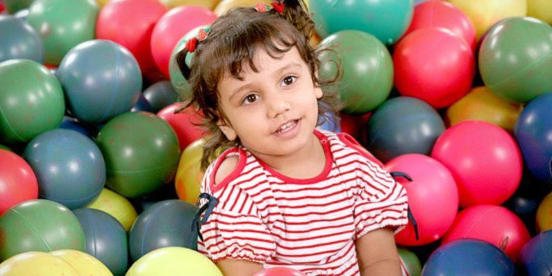 Little pretty girl is having fun indoor. Playing in children zone. Playing in colorful balls and smiling –  free photo